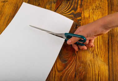 Makas, kağıt dokusunu kesiyor. Makasla el, beyaz kağıt parçası afişini fotokopi alanı üst görünümü ile keser