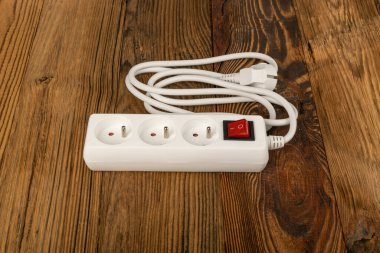 Tahta arka planda güç şeridi. Uzatma kablosu, elektrik kablosu, ev soketi, beyaz güç genişletici, ahşap döşemede uzatma kablosu