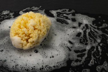 Natural sea sponge with soap foam on black background with copy space. Yellow sponge mockup, eco body care concept, eco friendly hygiene accessory mock up