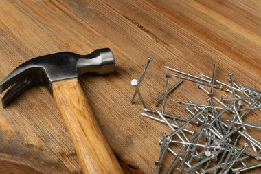 Metal nail pile and hammer on wooden desk. Steel nails on wood plate, construction hardware on brown wood background
