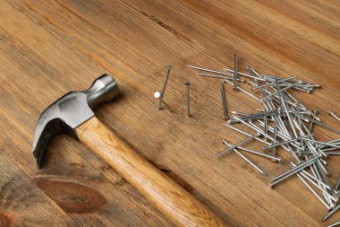 Metal nail pile and hammer on wooden desk. Steel nails on wood plate, construction hardware on brown wood background