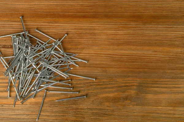 木製の机の上に金属釘杭 木板の鋼釘 茶色の木の背景に建設ハードウェア Top View — ストック写真