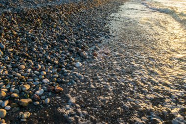 Sea waves on pebble beach texture background. Transparent ocean water, rocky shore pattern, summer mockup with copy space, stone shoreline, vacation concept