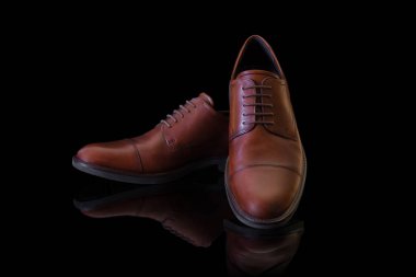 Siyah yansıtıcı yüzeyde bir çift markasız kahverengi, hakiki deri Oxford ayakkabısı. Ürün fotoğrafçılığı ve alışveriş konsepti