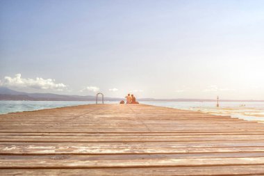 Rıhtımda oturan çift sallanan bacakları gölün üzerinde gün batımını izliyordu..