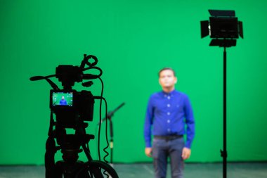 Saratov, Rusya - 4 Eylül 2018: Stüdyoda yeşil arka planda mavi gömlekli bir çocuğun videosu. Chromakey teknolojisi. Tripodun üzerinde bir mikrofon, tripodun üzerinde bir video kamera..