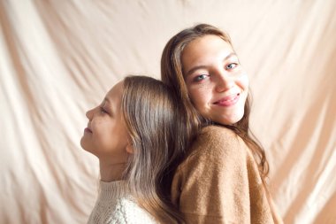 kız kardeşler bej renkli tekstil arka planında eğleniyorlar