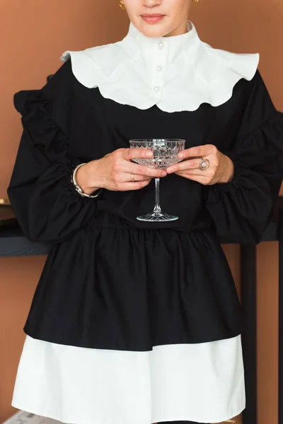 Ausgeschnittenes Bild einer Modefrau in einem schwarzen und weißen Kleid mit elegantem Glas für Cocktails — Stockfoto