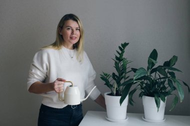 Kadın çiçekleri suluyor, kameraya bakıyor.