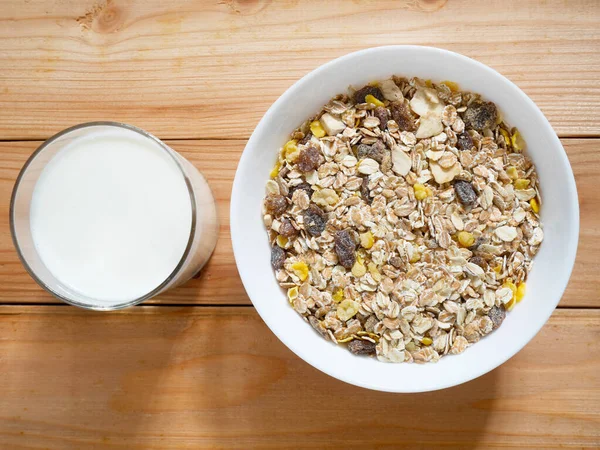 A Bowl of muesli breakfast and rolled oats with dried fruits and a glass of milk on wooden table. Top view.
