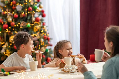 İki çocuklu mutlu anne, tatil için dekore edilmiş evin mutfağında zencefilli ekmekle çay içiyor. Mutlu Noeller ve mutlu Noeller. Sevgili bir aile Noel 'i kutlar.