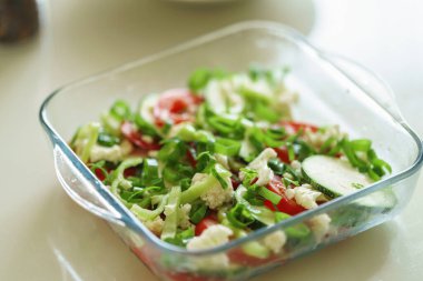 Cam formda taze sebze tabağı mutfaktaki ahşap masada duruyor. Sebzeli güveç, kabak, domates, düzgün beslenme. Sağlıklı kilo kaybı.