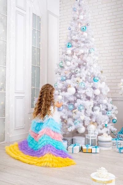 メリークリスマスと幸せな休日 空想のドレスの少女は巨大な白いクリスマスツリーを飾ることです ギフトボックスの隣の子供 おもちゃで装飾されたリビングルーム ホワイトハウスでの居心地の良い暖かい冬の日 — ストック写真