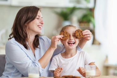 Sevgi dolu bir aile, anne ve kız, masada oturup sabahları kahvaltı yapmak. Kadın ve kız yulaf ezmeli kurabiye yer, inek sütü içer ve mutfakta güzel vakit geçirir.