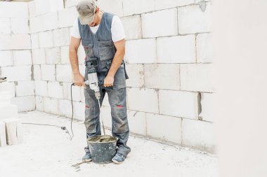 Genç erkek tuğla ustası beton yoğuruyor, havalanan beton bloklar döşemek için, inşaat alanında bir mikser kullanarak. Metin için boş alan. Boşluğu kopyala
