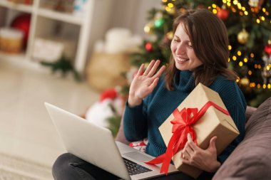 Genç bir kadın internet üzerinden iletişim kuruyor ve aldığı hediyeyi rahat bir Noel arifesinde dizüstü bilgisayarında gösteriyor. Kız kanepede oturuyor. Arka planda süslü bir Noel ağacı var..