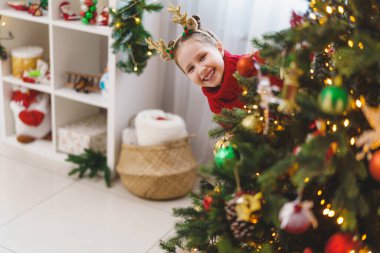 Evdeki Noel ağacını süsleyen küçük tatlı bir kız. Mutlu noeller. Kırmızı ceketli bir çocuk ağaca Noel ağacı oyuncağı asıyor..