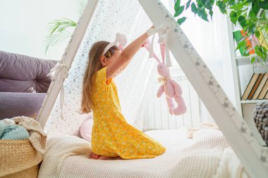 Küçük tatlı kız, oyuncak çadırında oturan tavşanların yumuşak oyuncaklarının kahramanlarıyla oynuyor. Çocuk evde. Çocukların hayali, mutlu çocukluk.