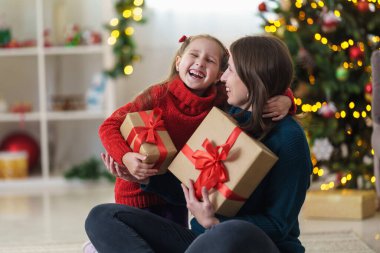 Mutlu Noeller ve mutlu tatiller. Mutlu anne-kız kucaklaşması ve arka planda süslenmiş Noel ağacının üzerinde Noel hediyesi kutusuyla beklemede kalın. Boşluğu kopyala