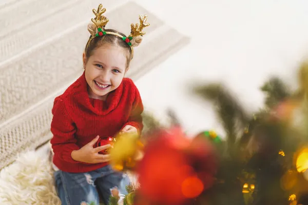 可爱的小女孩在家里装饰圣诞树 圣诞快乐 一个穿着红色夹克的孩子在树上挂着一个圣诞树玩具 — 图库照片