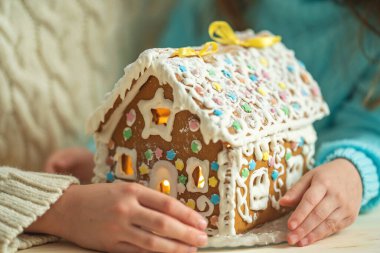 Yakın plan, çocuklar yıldız şeklinde şekerlerle süslenmiş el yapımı zencefilli kurabiye evi tutuyorlar. Tatil için hazırlanmış lezzetli kurabiyeler..