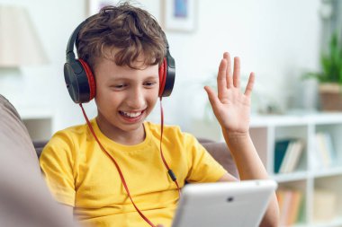 Kulaklığı ve tableti olan mutlu çocuk evinde, kanepede oturuyor. Çocuk evdeki arkadaşlarıyla internet tabletinde müzik dinleyerek iletişim kurmaktan mutlu. Çocuklara öğretmek için yeni bir uygulama.