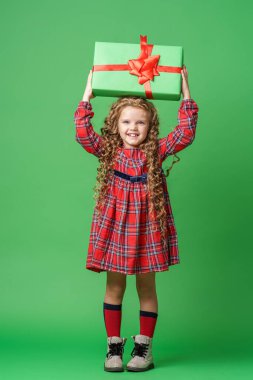 Yedi yaşında, sarı geyik boynuzlarıyla kıvırcık saçlı şirin bir kız. Stüdyoda yeşil bir arka planda hediye kutularıyla duruyor. Çocuk mutlu bir şekilde gülümser ve çerçeveye bakar. Reklamcılık. Boşluğu kopyala