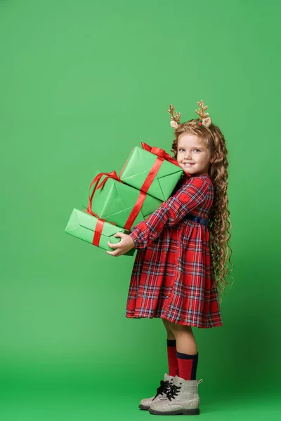 可爱的小女孩 卷曲的头发 金鹿角 坐在工作室绿色背景的礼品盒上 那孩子高兴地笑着 朝镜框里看去 — 图库照片