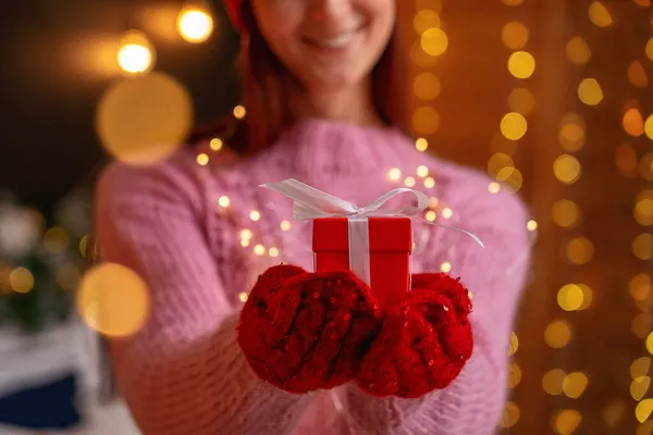 woman gives a Christmas gift box, holding it forward. Close up. gift pen close-up. Decorative red gift box, tied with a white ribbon and a bow, in the hands of a woman. On a new year\'s background.