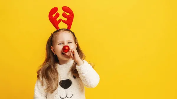 黄色の背景にトナカイの角とクリスマスボールの代わりに鼻でふわふわの白いセーターの幸せな女の子 子供は幸せで楽しくクリスマスの準備をしています スペースのコピー — ストック写真