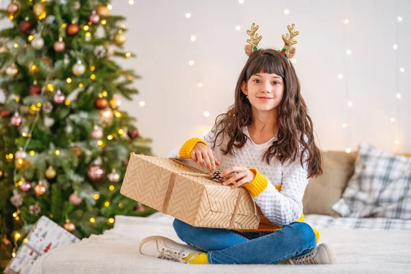 圣诞快乐 一个小女孩打开礼物 坐在一棵圣诞树下的床上 这个少年笑着欣赏这份礼物 — 图库照片