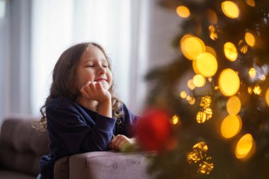 Mutlu noeller. Sevimli küçük bir kız evdeki bir odada Noel ağacı süslemeye hayran. Çocuk hayaller kurar ve yeni yılın parıldayan ışıklarına bakarak dilek tutar.