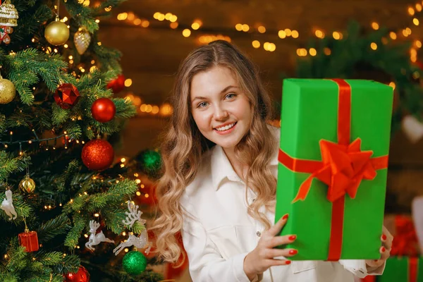 漂亮的女孩站在一棵装饰过的圣诞树的背景上 带着绿色礼品盒回家过节 那位年轻的女士高兴地笑了笑 看了看镜框 复制空间 — 图库照片
