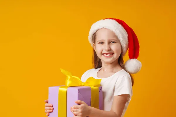 身穿白色T恤 头戴圣诞礼帽 快乐的小女孩在工作室里拿着一个黄色背景的圣诞礼品盒金字塔 孩子们笑着收到了许多圣诞礼物 — 图库照片
