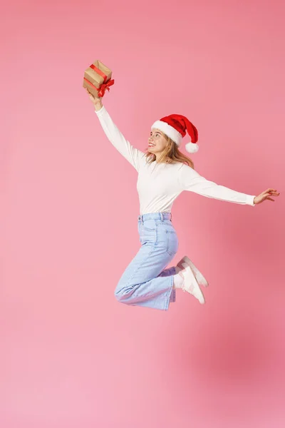 快乐的微笑着的女孩 手里拿着红丝带礼品盒 头上戴着一顶圣诞老人帽 背景是粉色的 准备圣诞节打折销售动态图像 — 图库照片