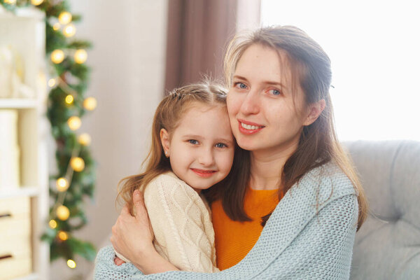 С Днем Матери. Маленькая дочь поздравляет свою мать и прижимается к ней, завернутая в одеяло, сидя на заднем плане огней. Мама и девочка улыбаются и обнимаются. Семейный отдых и единство.