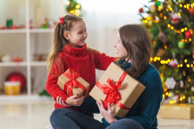 Mutlu Noeller ve mutlu tatiller. Mutlu anne-kız kucaklaşması ve arka planda süslenmiş Noel ağacının üzerinde Noel hediyesi kutusuyla beklemede kalın. Boşluğu kopyala