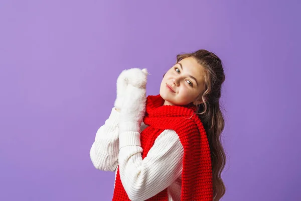 白いセーターとふわふわのミトンを着た魅力的なかわいい女の子がスタジオの紫色の背景に立っています 10代の女の子が楽しそうに笑顔で手を握っている コピースペース — ストック写真