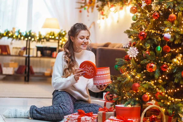 圣诞快乐 新年快乐 一位穿着白色毛衣的漂亮女人正坐在圣诞树旁的一座装饰过的房子里 她带着礼品盒 — 图库照片