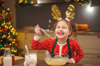 Bir çocuk Noel arifesinde mutfakta yemek hazırlar. Önlüklü bir kız hamurun malzemelerini bir kasede karıştırıyor. Mutlu Noeller ve mutlu Noeller. İçi Noel ışıklarıyla süslenmiş..