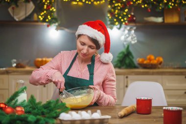 Bir kadın Noel arifesinde mutfakta yemek hazırlar. Önlüklü bir kız hamurun malzemelerini bir kasede karıştırıyor. Mutlu Noeller ve mutlu Noeller. İçi Noel ışıklarıyla süslenmiş..