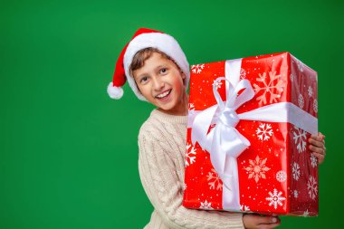 Yeşil arka planda Noel Baba şapkalı mutlu çocuk. Çocuk mutlu ve elinde büyük bir hediye tutuyor. Yeni yıl satışları, reklamlar, indirimler. Boşluğu kopyala.