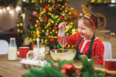 Bir çocuk Noel arifesinde mutfakta yemek hazırlar. Önlüklü bir kız hamurun malzemelerini bir kasede karıştırıyor. Mutlu Noeller ve mutlu Noeller. İçi Noel ışıklarıyla süslenmiş..