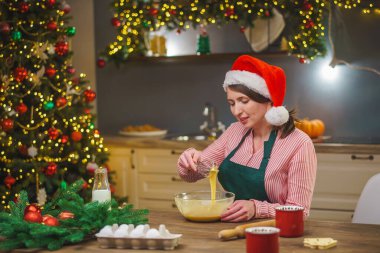 Bir kadın Noel arifesinde mutfakta yemek hazırlar. Önlüklü bir kız hamurun malzemelerini bir kasede karıştırıyor. Mutlu Noeller ve mutlu Noeller. İçi Noel ışıklarıyla süslenmiş..