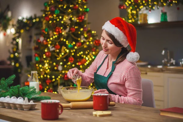 Bir kadın Noel arifesinde mutfakta yemek hazırlar. Önlüklü bir kız hamurun malzemelerini bir kasede karıştırıyor. Mutlu Noeller ve mutlu Noeller. İçi Noel ışıklarıyla süslenmiş..