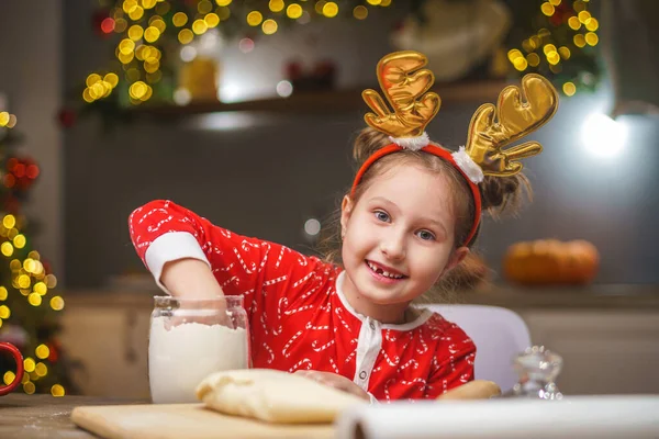 圣诞节前夕 一个孩子在厨房准备食物 一个穿围裙的女孩把面团搅拌在一起 加入面粉 圣诞快乐 节日快乐 内部装饰有圣诞灯饰 — 图库照片