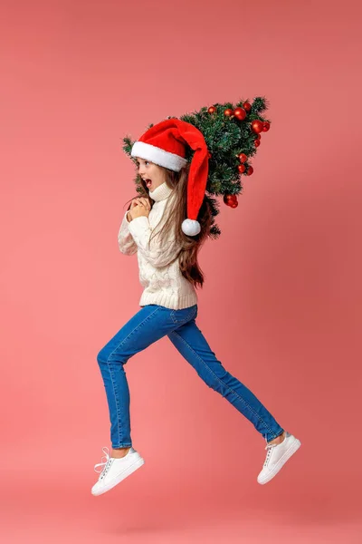 身穿针织毛衣 头戴圣诞帽 肩上挂着红色圣诞彩球的快乐少女 背着粉色背景走路 动态图像 — 图库照片