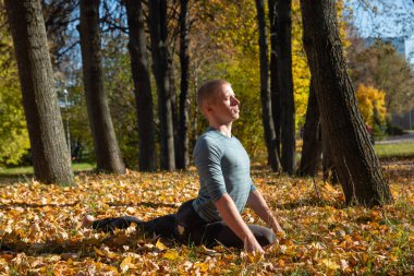Sonbahar parkında yoga yapan sporcu adam. 