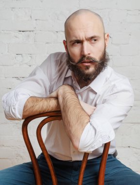 Portre, sakallı ve bıyıklı beyaz kel bir adam. Odada bir sandalyede oturuyor., 