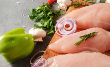 Otlu çiğ tavuk filetosu, kesme tahtasındaki soğan, tuz, maydanoz, mantar, biber.